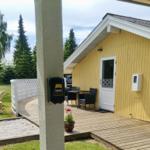 Haus mit Terrasse, Tisch, Stühlen und Sandkasten. Hintergrund: Gras, Bäume.