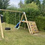 Holzspielgerüst mit Rutsche, Kletterwand und Reifen-Schaukel im Garten.