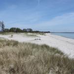Weißer Sandstrand mit Dünen und Windkraftanlagen im Hintergrund.