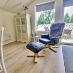 Ein Raum mit blauem Sessel, Holzboden und Blick auf die Terrasse.