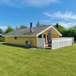 Gelbes Ferienhaus mit Terrasse und Garten unter blauem Himmel.