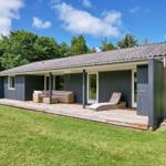 Ein modernes Haus mit Holzterrasse und Gartenmöbeln unter blauem Himmel.