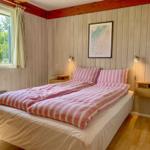 Schlafzimmer mit Doppelbett, Holzwand und Fensterblick auf Wald.