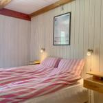 Schlafzimmer mit Bett, rosa Bettwäsche, Holzwand und Wandlampen.