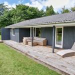 Terrasse mit Sitzgruppe und Liegestuhl neben Haus mit Holzdecke und grünem Rasen.