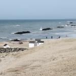 Strand mit weißen Hütten, Felsen und einem roten Boot.