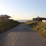 Straße entlang der Küste mit Häusern und Warnschild