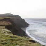 Meer an der Klippe mit Leuchtturm im Hintergrund.
