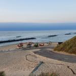 Strand mit Fischerbooten und Dünen im Hintergrund.