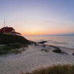 Haus mit rotem Dach auf Dünen über Strand bei Sonnenuntergang