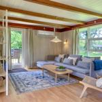 Wohnzimmer mit Sofa, Tisch und Teppich. Holzdecke und große Fenster.