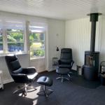 Zimmer mit zwei schwarzen Sesseln, Kamin und Fenstern zum Garten.