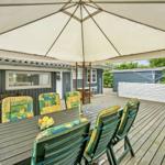 Terrasse mit Tisch, Stühlen und Sonnenschutz. Hintergrund: Haus und Grün.