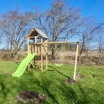 Holzspielplatz mit Rutsche und Schaukel auf grünem Rasen