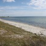 Strand mit weißen Steinen und Windkraftanlagen am Horizont.