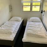 Zwei Betten mit weißen Bettwäschen und Decken. Fenster mit Blick auf Grünfläche.