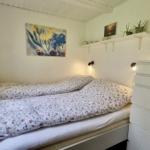 Schlafzimmer mit Bett, Fenster, Wandbild und weißen Regalen.