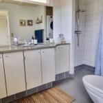 Badezimmer mit Dusche, Waschbecken und Toilette. Fliesenboden und Holzmatte.