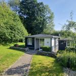 Ein kleines Haus mit dunklem Holz und weißer Fassade, umgeben von Grün und Bäumen.