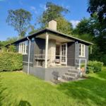 Ein graues Haus mit Veranda und Garten. Umgeben von Bäumen und Gras.