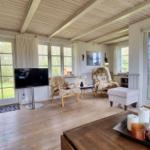 Wohnzimmer mit Holzboden, TV, zwei Sessel und großen Fenstern.