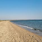 Strand mit Sand und ruhigem Meer unter blauem Himmel