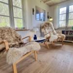 Zwei Sessel mit Felldecken, Couchtisch und Bücherregal im Wohnzimmer.