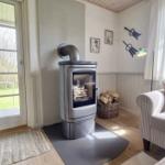 Wohnzimmer mit Kaminofen, Sofa und Blick auf die Terrasse.