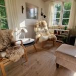 Zwei Stühle mit Felldecken, Tisch und Sessel im Raum mit Fenstern.