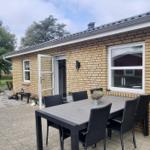 Terrasse mit Tisch und Stühlen vor einer Backsteinfassade mit offener Tür.