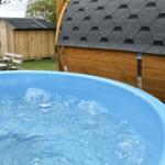 Blauer Whirlpool mit sprudelndem Wasser im Garten neben einem Holzhaus.