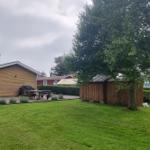 Grüner Garten mit Holzsauna, Grill und Picknicktisch. Hintergrund: Haus und Bäume.