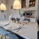 Essbereich mit Tisch, Stühlen und Küchenbereich im Hintergrund.