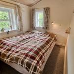 Schlafzimmer mit Doppelbett, zwei Fenstern und Holzdecke.