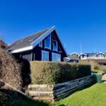 Schwarzes Holzhaus mit weißem Fensterrahmen und Dachgauben. Grünflächen und Hecke im Vordergrund.