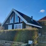 Schwarzes Holzhaus mit weißen Fensterrahmen und Dach, umgeben von Hecken und Grünflächen.