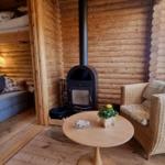 Wohnbereich mit Kamin, Sessel und Tisch. Im Hintergrund Schlafzimmer mit Sofa und Bett.