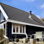 Schwarzes Holzhaus mit weißen Fensterrahmen und Terrasse mit Gartenmöbeln.