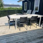 Terrasse mit Tisch, Stühlen und Grill neben schwarzem Haus.