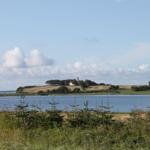 Blick auf einen See mit Insel, auf der ein Leuchtturm und Gebäude stehen.