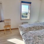 Schlafzimmer mit Doppelbett, Stuhl und Fenstern zur Aussicht.