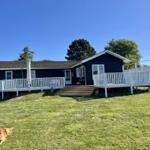 Schwarzes Ferienhaus mit weißer Veranda und Grünfläche. Ein Hund liegt im Vordergrund.