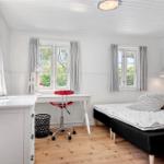 Zimmer mit Bett, Schreibtisch und Fenstern mit Vorhängen.