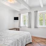 Schlafzimmer mit Bett, Fenstern und Terrakottboden.