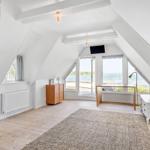 Dachgeschosszimmer mit großem Fenster, Holzboden und weißem Mobiliar.