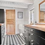 Badezimmer mit Holzwaschtisch, schwarz-weißem Boden und Holztür.