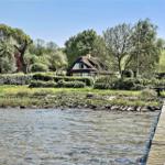 Haus mit Strohdach am Wasser mit Steg und Grünflächen.