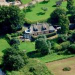 Dorfhaus mit Schieferdach, umgeben von Grünflächen und Bäumen. Flussufer im Vordergrund.