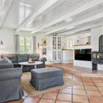 Wohnzimmer mit Sofa, Sitzbank und Kaminofen. Holzboden und weiße Deckenbalken.