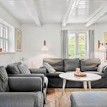 Wohnzimmer mit grauem Sofa, runden Tisch und Fenstern.